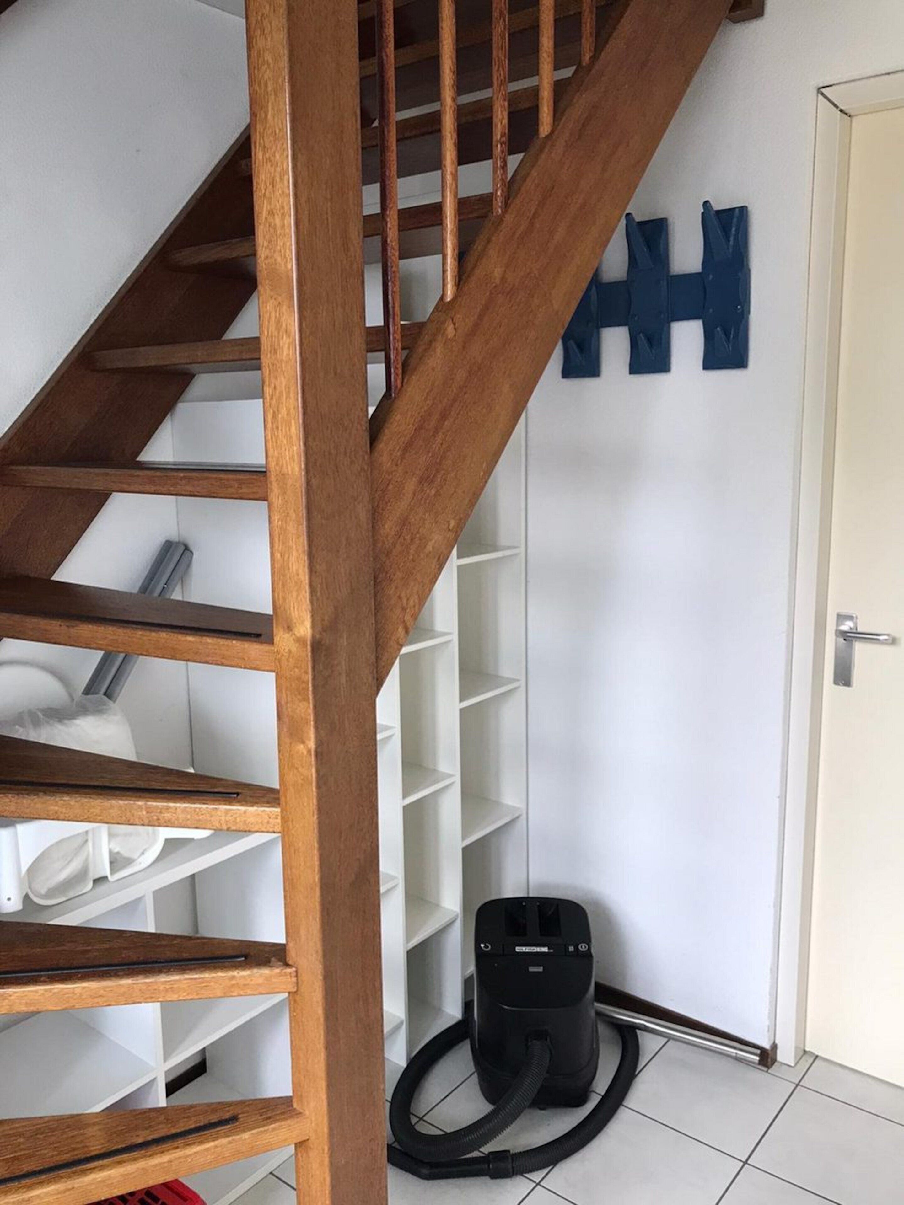 A wooden staircase leading to a white room with a vacuum cleaner on the floor.
