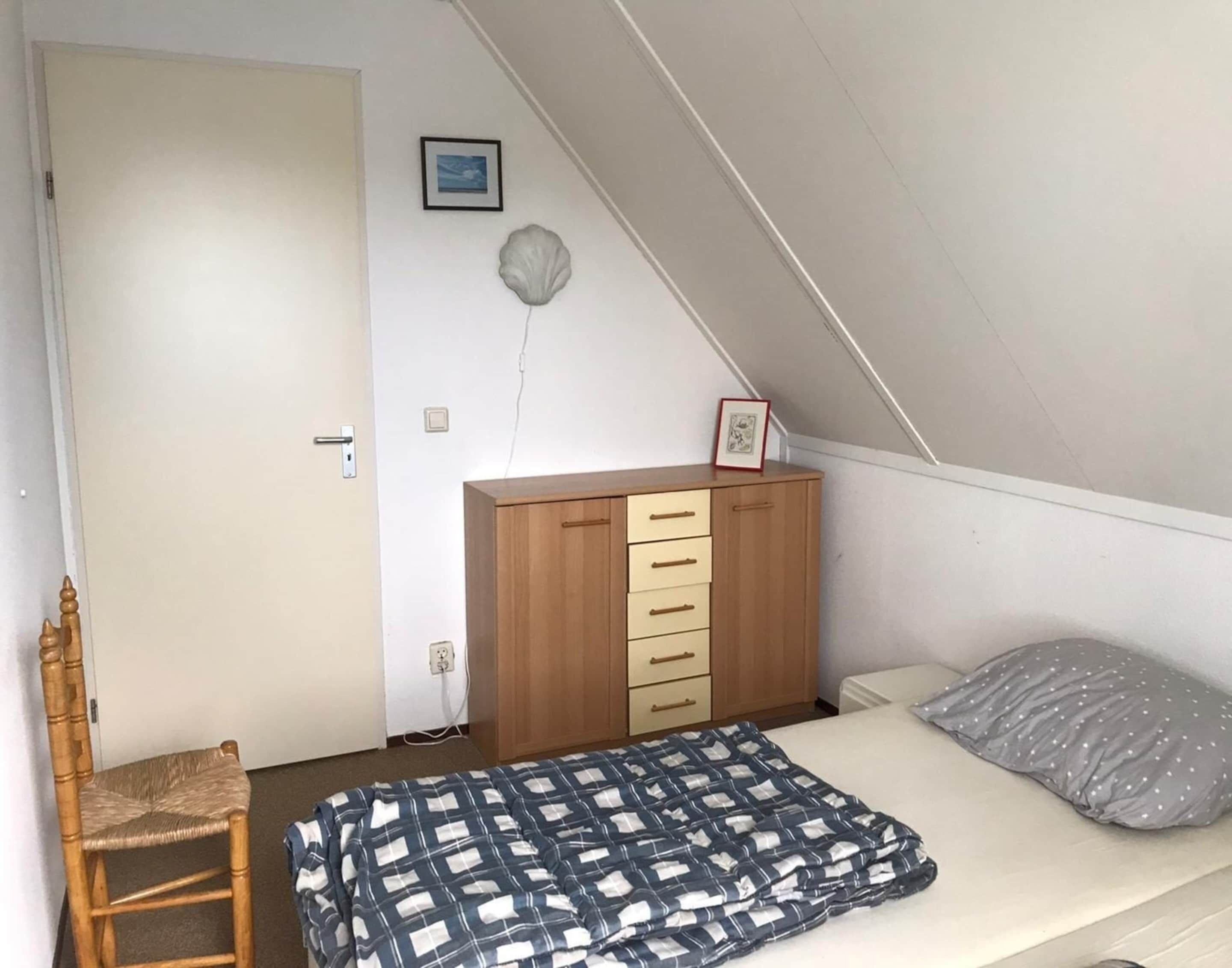 Una camera da letto con un letto, una cassettiera in legno, una sedia e uno scaffale a parete.