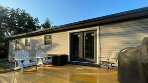 A single-story house with a covered deck, two Adirondack chairs, a small table, and a grill.