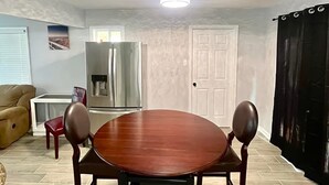 A dining area with a round table, two chairs, a refrigerator, and a door.