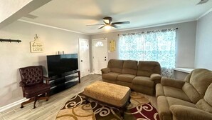 A living room with a television, leather armchair, sofa, ottoman, and patterned rug.
