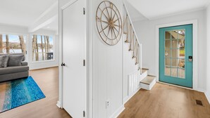 Un intérieur moderne avec un escalier, une porte de couleur turquoise et une vue sur les arbres à travers de grandes fenêtres.