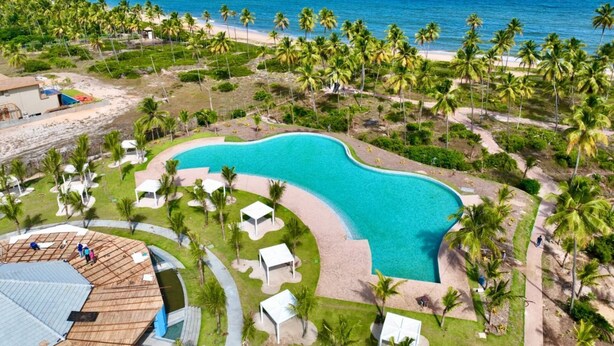 Ein Resort mit großem Schwimmbad, Palmen und einem Strand.