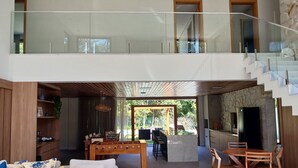 Ein geräumiger Wohnbereich mit hohen Decken, einem Esstisch, Sofas und einer Küchenzeile mit Steinwand und modernen Geräten.