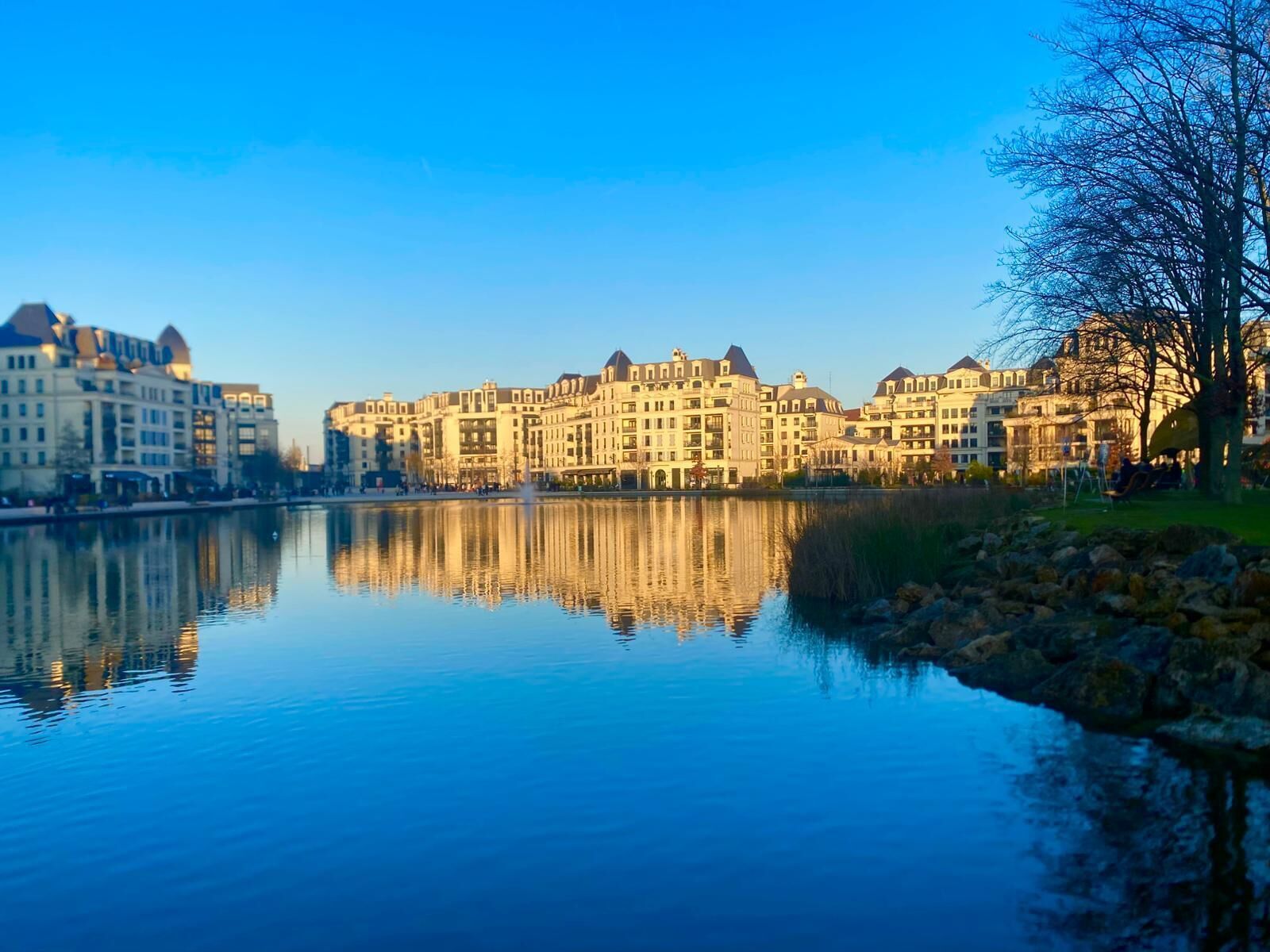A waterfront hotel with multiple buildings reflecting on the calm water.