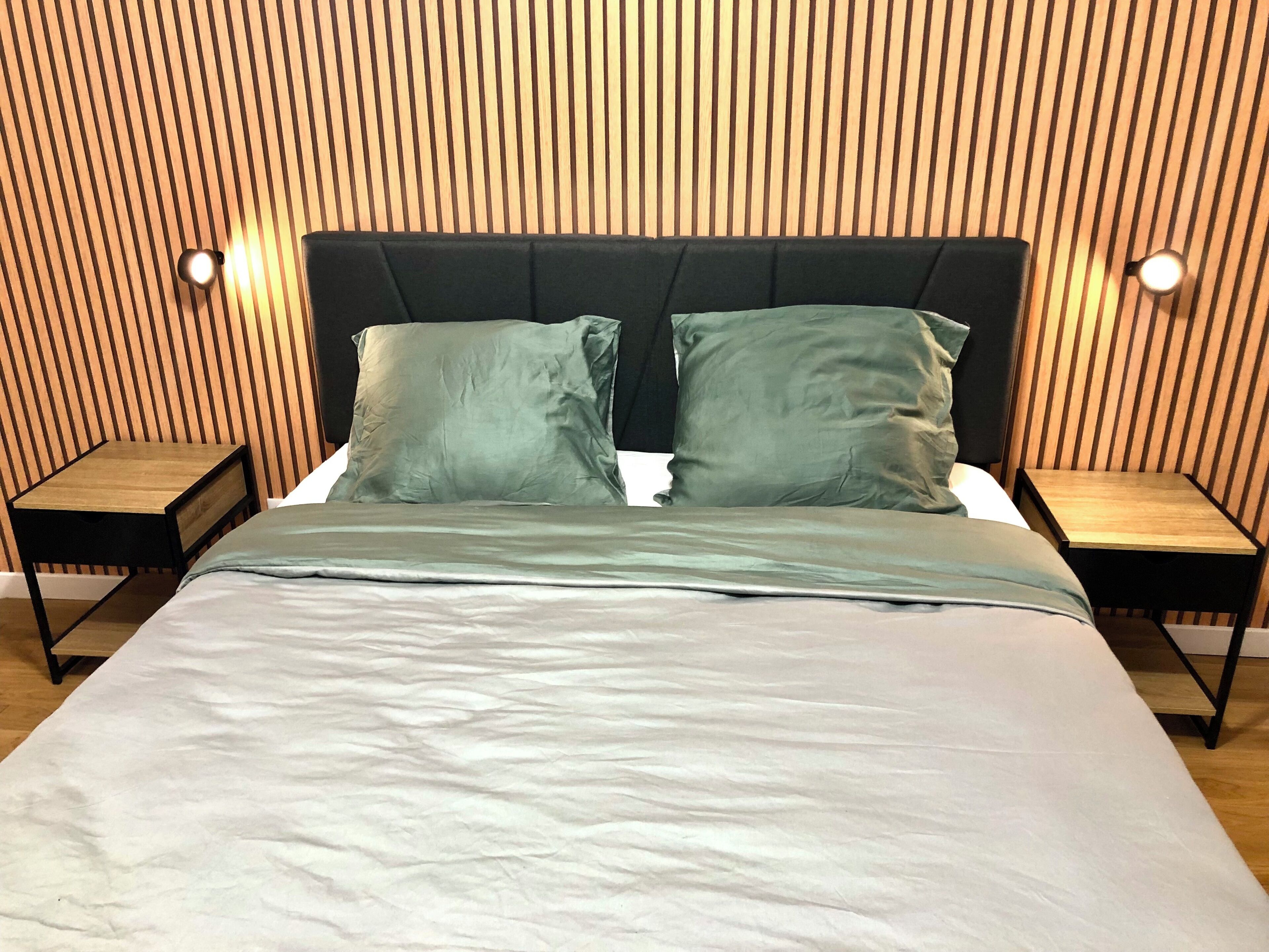 Una cama con cabecera de madera, dos almohadas y una mesita de noche con una lámpara.