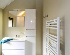 Une salle de bain moderne avec un lavabo blanc, un miroir et un porte-serviettes.