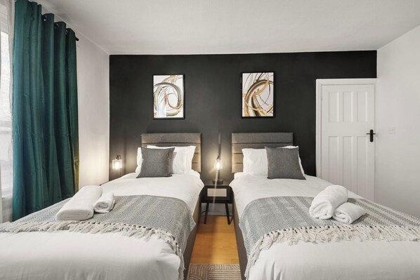 A hotel room with two beds, a nightstand, a door, and artwork on the walls.