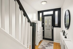 A hallway with a white staircase, a door with a black frame, a white cabinet, and a mirror on the wall.