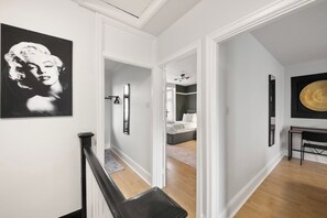 A hallway with a staircase, a bed, and a dining area.