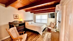 A bedroom with a wooden ceiling, a bed, a dresser, a chair, a TV, and a window. - Cottage 34: Coconut Cottage - Waterfront Lodging in Downtown Tavares, FL (Tavares)