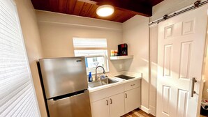 A compact kitchen with a stainless steel refrigerator, a sink, and a wooden floor. - Cottage 34: Coconut Cottage - Waterfront Lodging in Downtown Tavares, FL (Tavares)