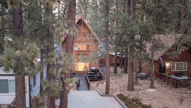 Une cabane aux murs en bois, entourée de pins, dotée d’une terrasse à l’avant et d’un espace extérieur aménagé et couvert.