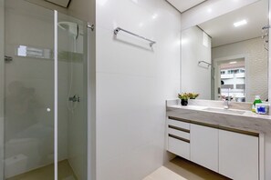 Un bagno moderno con box doccia in vetro, mobile lavabo bianco con piano in marmo e un grande specchio.