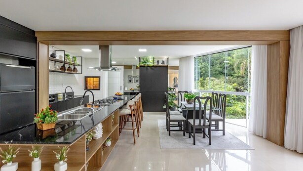 A modern kitchen with a central island, bar stools, and a dining area with a view of greenery.