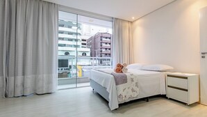 A modern hotel room with a large window, a bed with a floral bedspread, a bedside table, and a view of the cityscape.