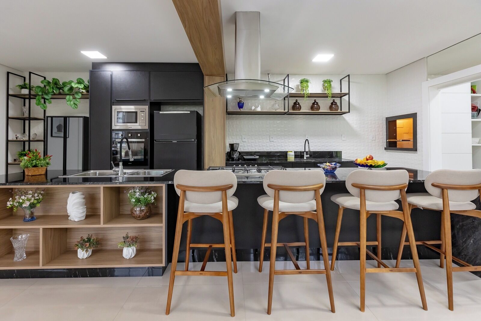 Eine moderne Küche mit schwarzen Schränken, einem Edelstahlkühlschrank, einer Mikrowelle und einem Gasherd. Holzhocker und ein Regal mit Pflanzen sind ebenfalls vorhanden.