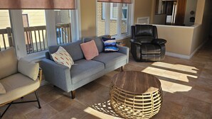 Un salon avec un canapé gris, un fauteuil en cuir noir, un pouf en osier et une petite table.