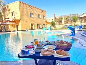 A poolside breakfast setup with various food items and a pool in the background. - Giza palace hotel pyramids view (Giza)