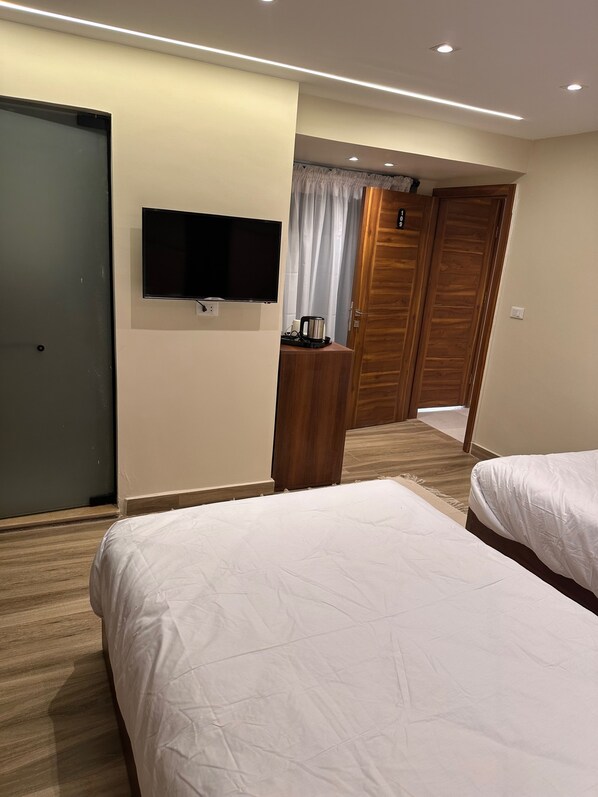 A hotel room with two beds, a TV mounted on the wall, a wooden dresser, and a wooden wardrobe. - Giza palace hotel pyramids view (Giza)