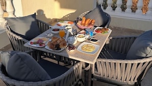 A dining table with a variety of food items on a rooftop terrace with a view of buildings and a pyramid in the background.