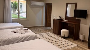 A hotel room with two beds, a desk, a TV, and an air conditioning unit.
