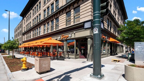 Een gebouw met een restaurant genaamd 'Snooze', met terrasstoelen en oranje parasols.