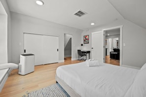 Un dormitorio moderno con cama, escritorio, silla y armario blanco.