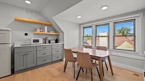 Een keuken met grijze kastjes, een houten tafel, stoelen, een magnetron en een raam met jaloezieën.