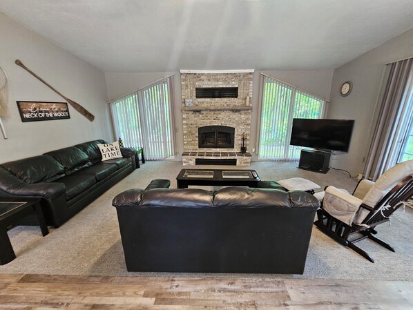 A living room with a fireplace, a black leather sofa, a wooden coffee table, and a television. - Lakeside Serenity Meets Northern Adventure, Stunning Sunsets, Family Getaway! (Nevis)