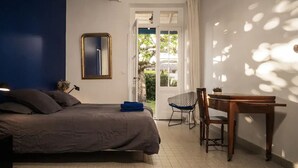 Ein Schlafzimmer mit einem Bett, einem Schreibtisch und einem Stuhl. Eine Tür führt zu einem Außenbereich.