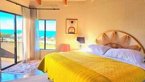 Un dormitori amb un llit gran, una decoració de estrella de mar, una làmpada i vista a l'oceà a través d'una finestra.
