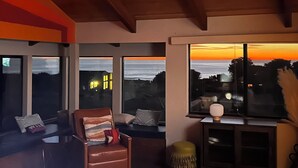 Una habitació amb grans finestres, sostre de fusta i vista al capvespre.