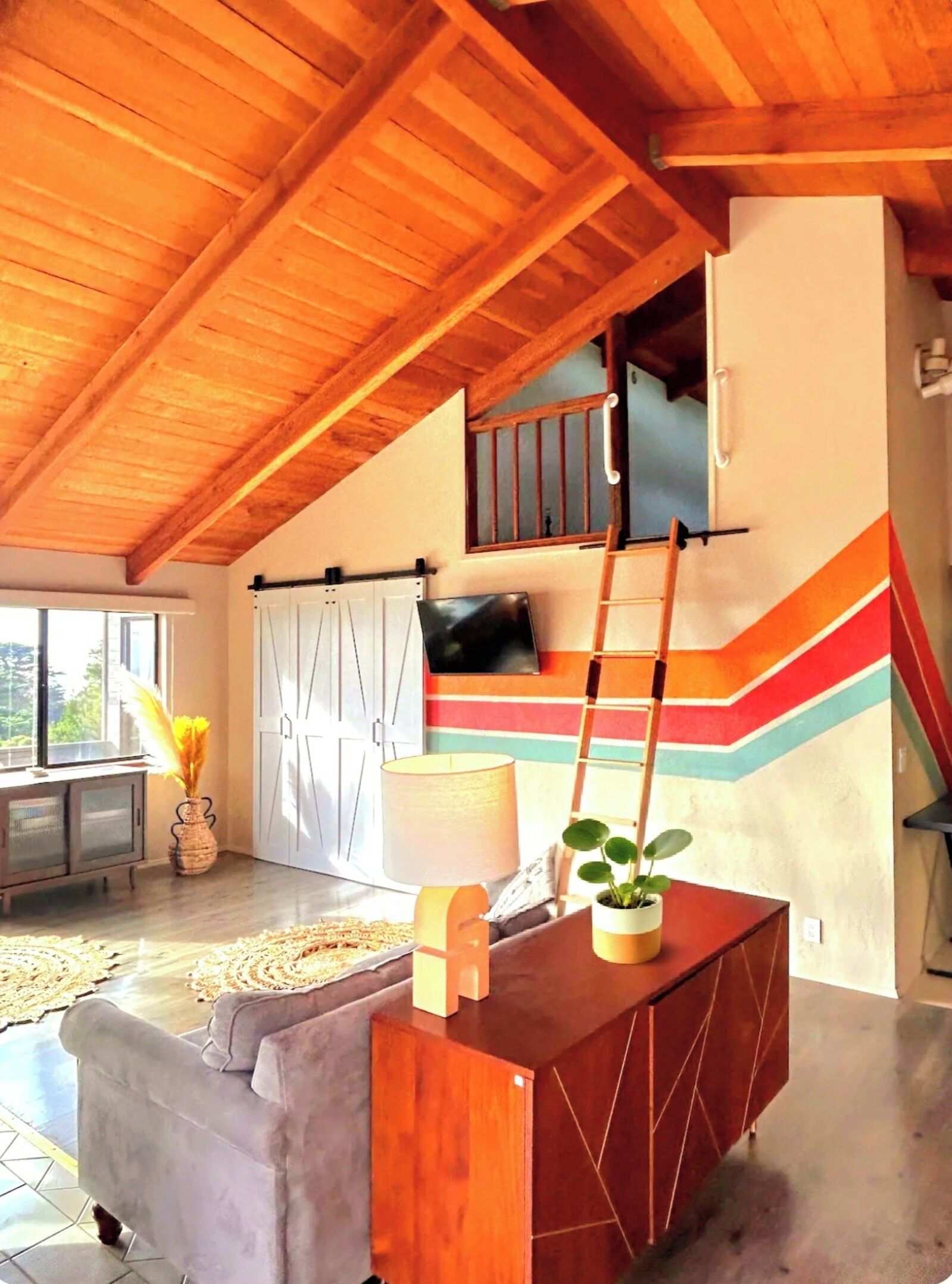 A spacious living area with a high ceiling, a staircase, and a television mounted on the wall.