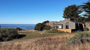 Una casa moderna amb vistes a l'oceà, envoltada de paisatge natural i arbres.