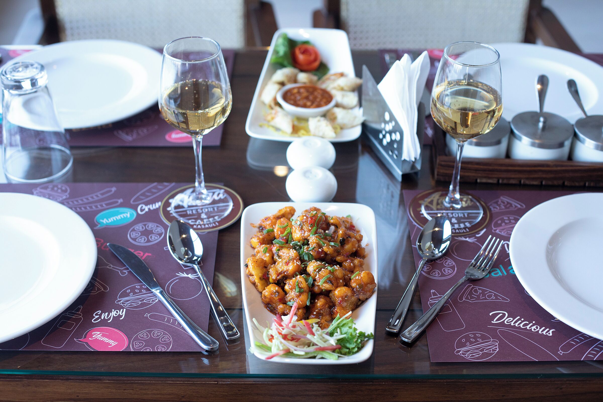 A dining table set with plates, cutlery, glasses, and a central dish of food.