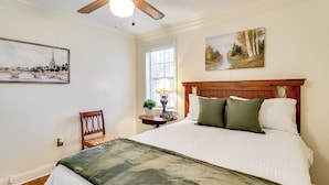 A bedroom with a bed, a chair, a nightstand, a lamp, and artwork on the walls. - 3 Mi to Mississippi Stadium: Cozy Jackson Getaway! (Jackson)