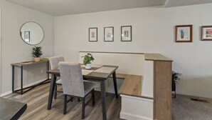 Ein Essbereich mit Tisch, Stühlen, einer Pflanze und gerahmten Bildern an der Wand.