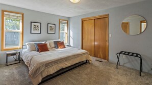 Ein Schlafzimmer mit einem Bett, zwei Fenstern, einer Holztür, einem Spiegel und einem kleinen Tisch.