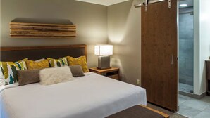 Una habitación de hotel con una cama grande, una mesita de noche con lámpara, un banco de madera, un armario y una puerta al baño.