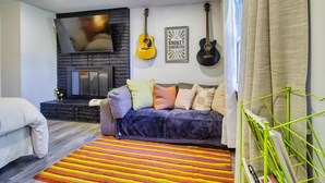 A cozy living room with a fireplace, a sofa with cushions, a colorful striped rug, and two guitars on the wall.