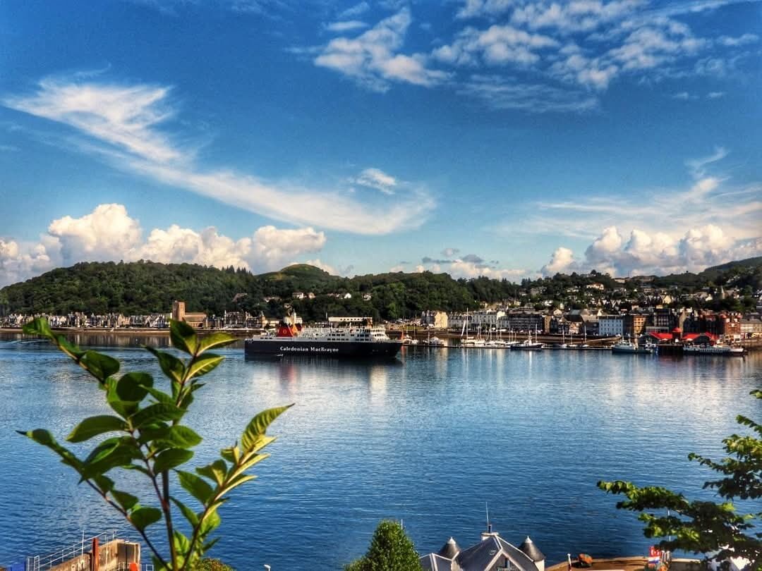 En havn med et stort skib, en bysilhuet i baggrunden og en klar himmel.