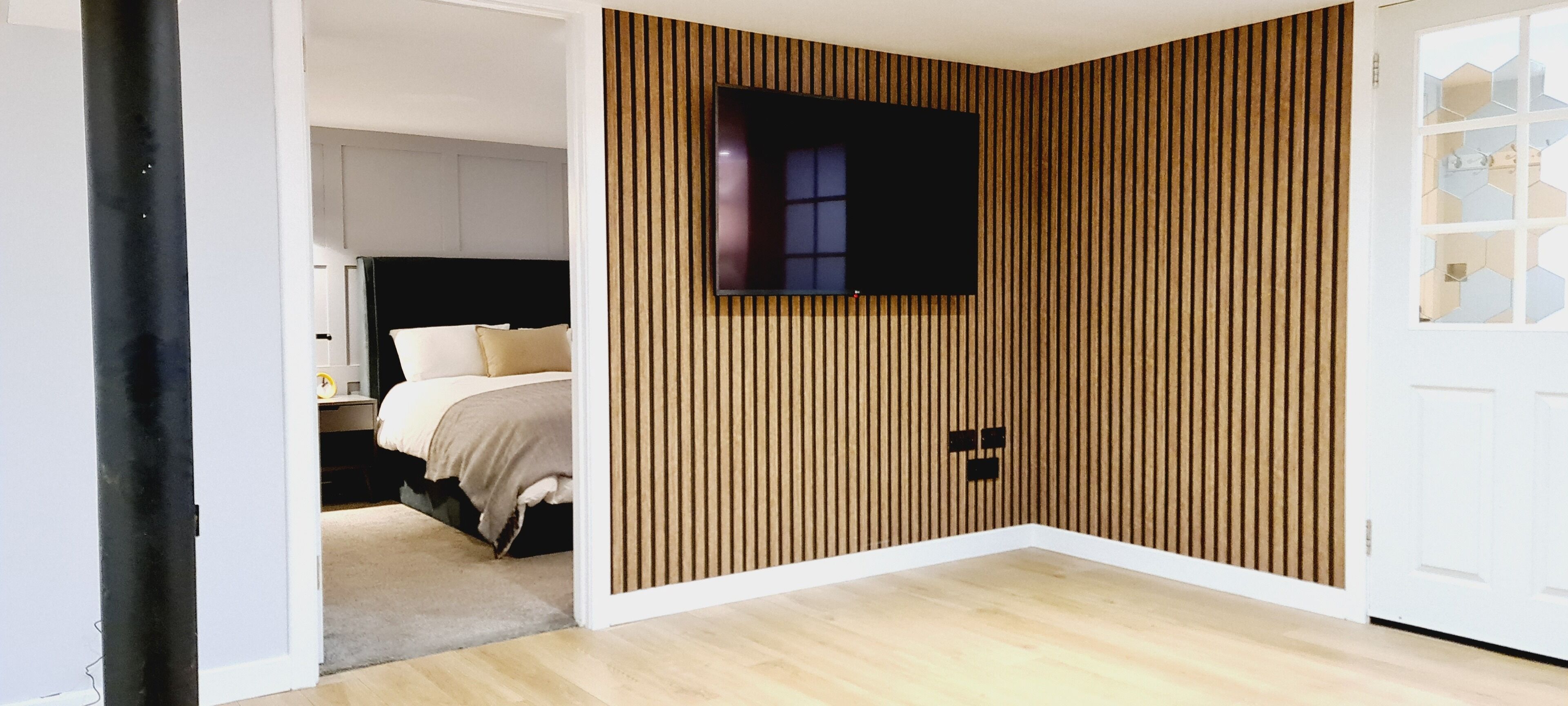 Un dormitorio con cama, televisor montado en la pared y diseño de pared con listones de madera.