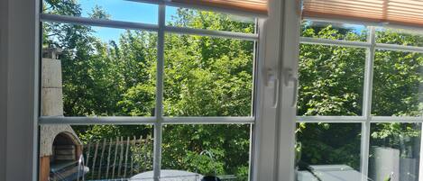 A room with large windows, a view of greenery outside, and a metal rack with items on it.