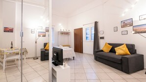 A modern living room with a grey sofa, a small table with a bottle, and a TV on a stand. - La Dolce Vita Apartment - metro Jonio (Roma)