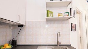 A kitchen with a stainless steel sink, a fruit bowl, and a shelf with a green bag and a box. - La Dolce Vita Apartment - metro Jonio (Roma)