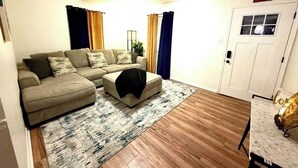 Un salon comprenant un ensemble de canapés, une table basse, un tapis, des rideaux et une porte avec un panneau indiquant la sortie.