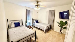 Une chambre avec deux lits, un ventilateur de plafond, une télévision et une plante en pot.