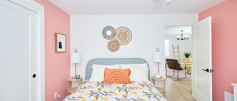 Ein Schlafzimmer mit Bett, Nachttischen, Deckenventilator und einer Tür zu einem anderen Raum.