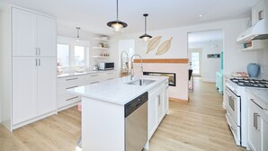 Una cocina moderna con armarios blancos, una isla central con pileta, estufa y lavavajillas. Hay luces colgantes sobre la isla y un microondas en la encimera.
